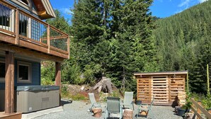 A wooden deck with outdoor seating, a hot tub, and a wooden structure in a forested area. - The Snowshoe House - 3 bed 2 bath cabin + hot tub (Agassiz)