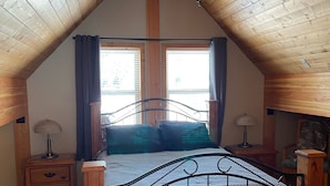 A bedroom with a sloped ceiling, a bed with a metal frame, two bedside tables with lamps, and a window with curtains. - The Snowshoe House - 3 bed 2 bath cabin + hot tub (Agassiz)