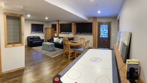 A cozy living room with a shuffleboard table, a fireplace, and a view of the outdoors through a window. - The Snowshoe House - 3 bed 2 bath cabin + hot tub (Agassiz)