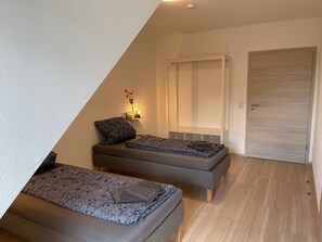 Une chambre avec deux lits, une table de chevet avec une lampe, une armoire et une petite fenêtre donnant sur un paysage agréable.
