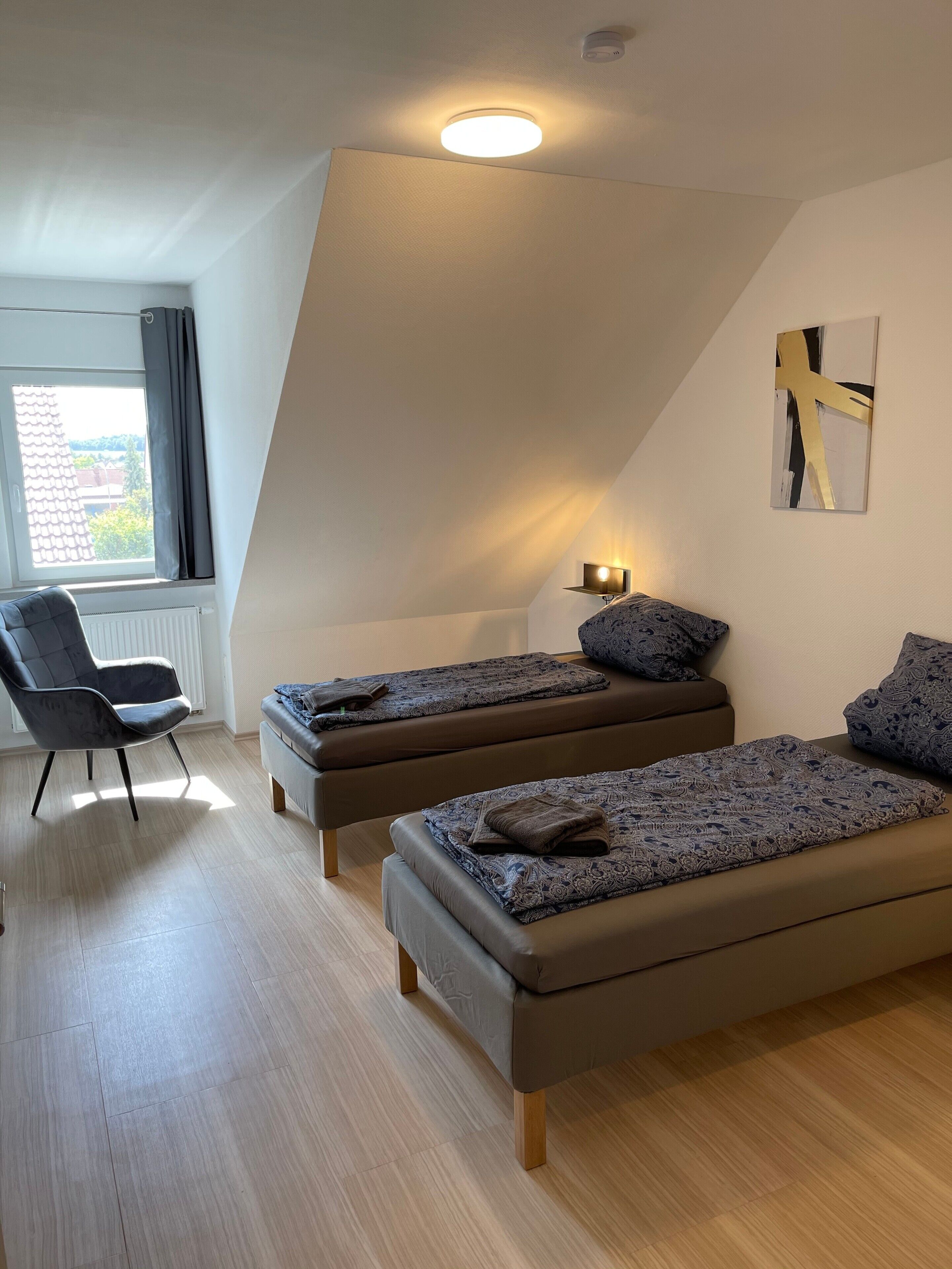 Une chambre moderne avec deux lits, une chaise, une fenêtre et un luminaire au plafond.