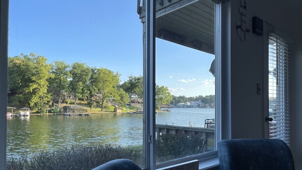 Ett rum med ett stort fönster med utsikt över en sjö, en stol, ett litet bord och en skylt med texten ”Njut av dagen”.