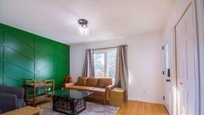 Ein Wohnzimmer mit einer grünen Akzentwand, einem braunen Sofa, einem Glastisch und einem Korbtisch.