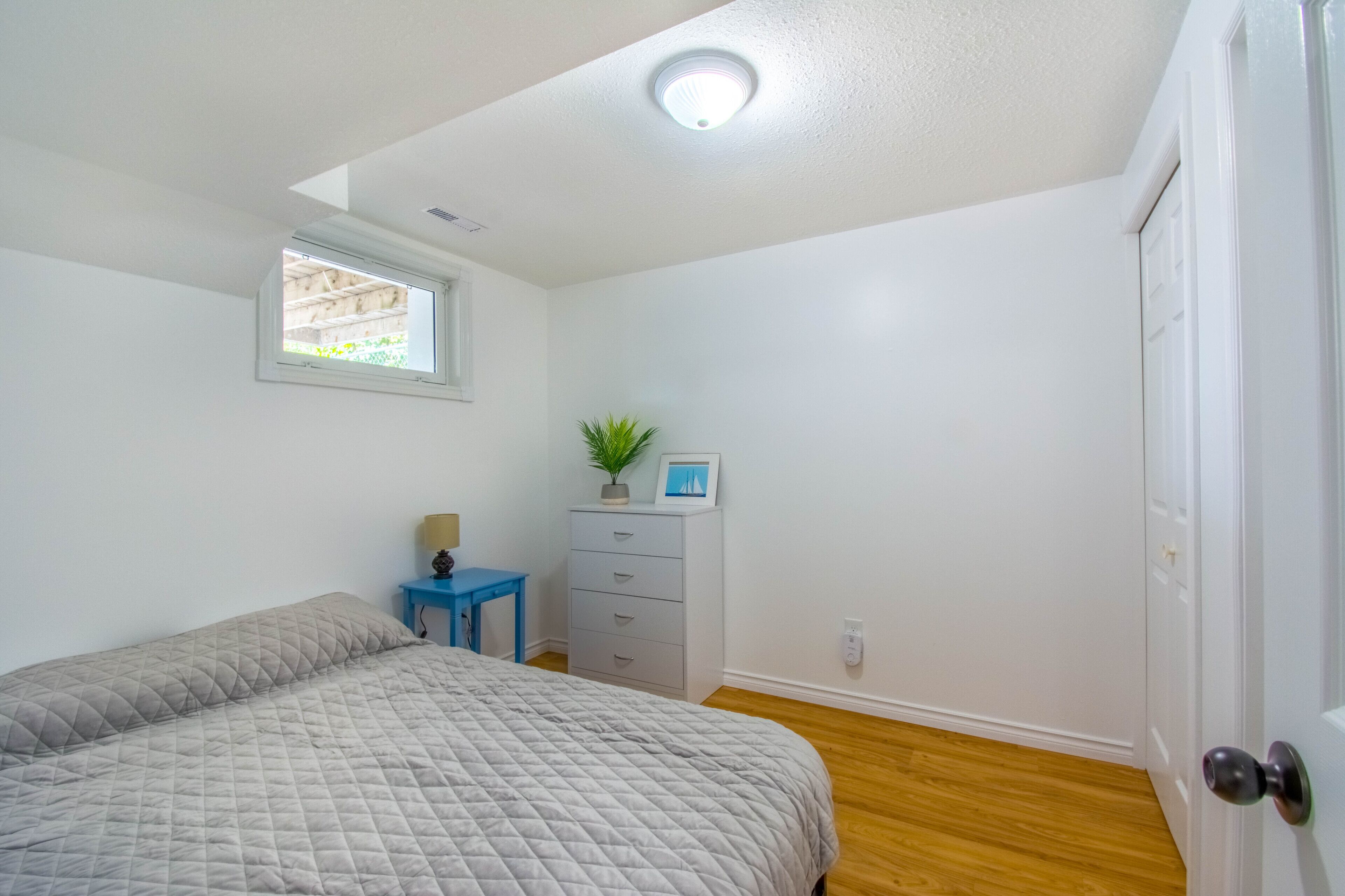 Un dormitorio con cama, cómoda, mesita y ventana.