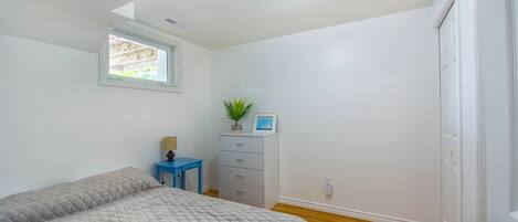 Un dormitorio con cama, cómoda, mesita y ventana.