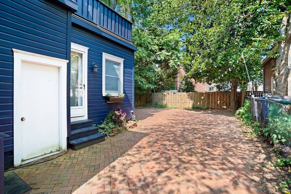 A residential property with a paved driveway leading to a front door, a wooden fence, and a backyard with a tree.