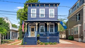 Une maison bleue à deux étages, avec un porche à l’avant, un drapeau et une enseigne.