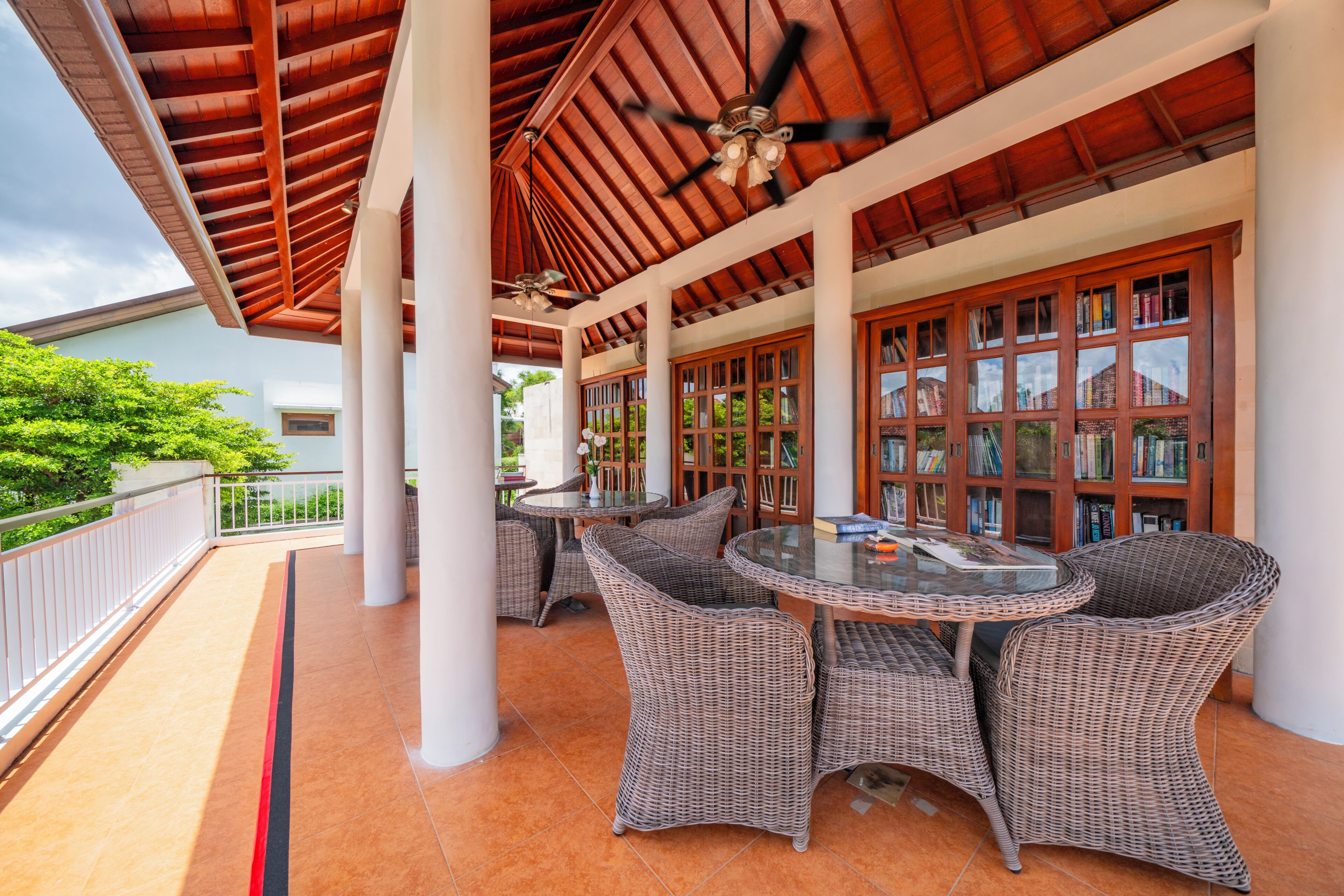 A covered outdoor area with wicker furniture, ceiling fans, and a bookshelf.