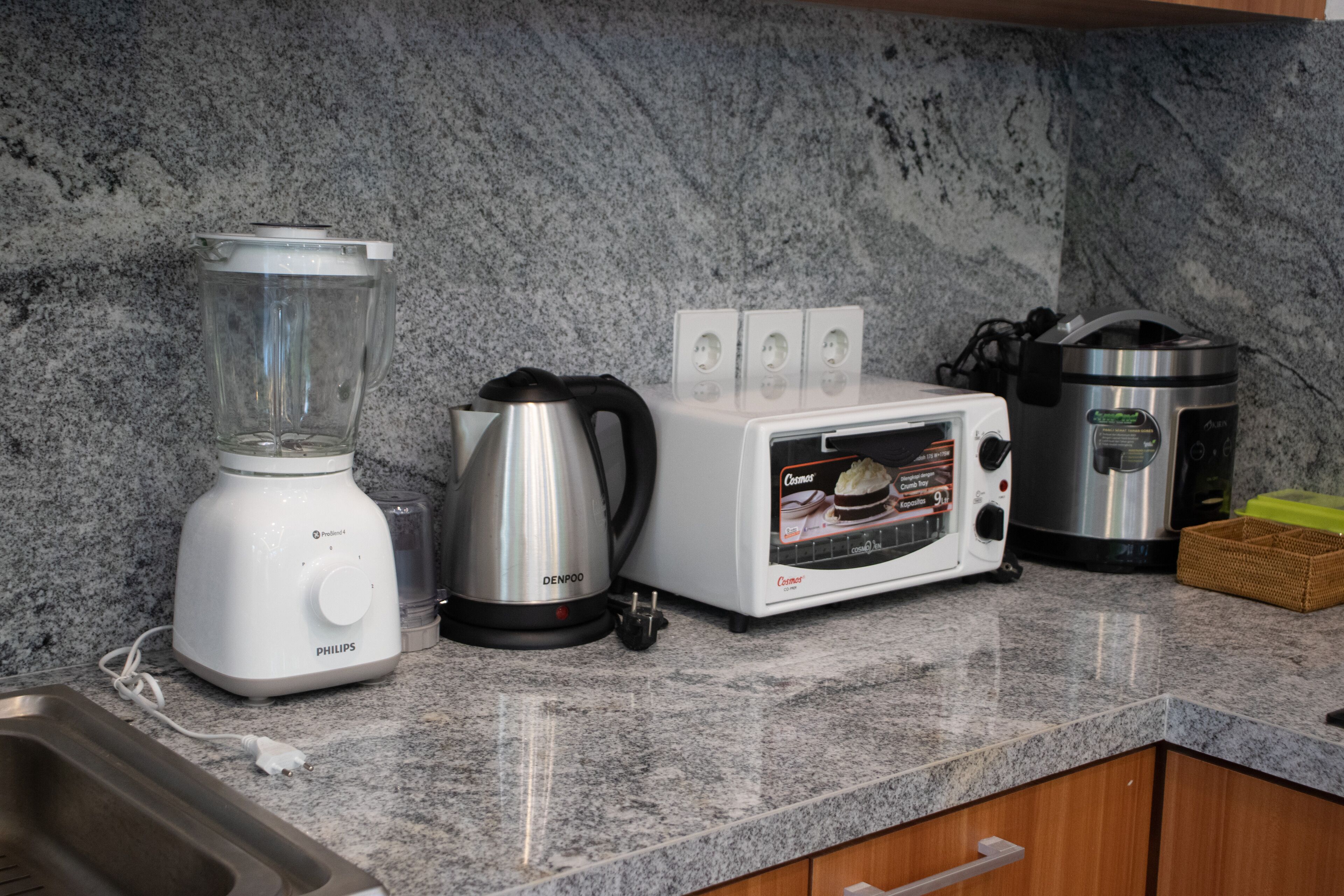 Una cocina con licuadora, tostadora, hervidor y cafetera sobre una encimera de granito.