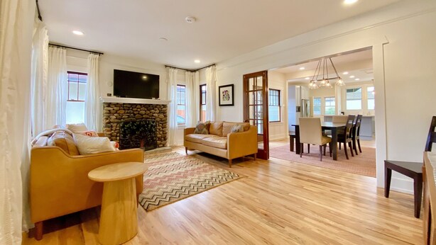 A spacious living room with a fireplace, a television mounted above it, and a dining area with a table and chairs. - Fully Renovated, Charming Craftsman Home in Downtown Paso Robles Wine Country (Paso Robles)