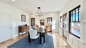 A spacious dining area with a large wooden table, white chairs, and a blue patterned rug. - Fully Renovated, Charming Craftsman Home in Downtown Paso Robles Wine Country (Paso Robles)
