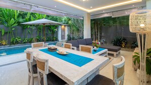 Ein moderner Essbereich im Freien mit Pool, Holzmöbeln und üppiger Bepflanzung.