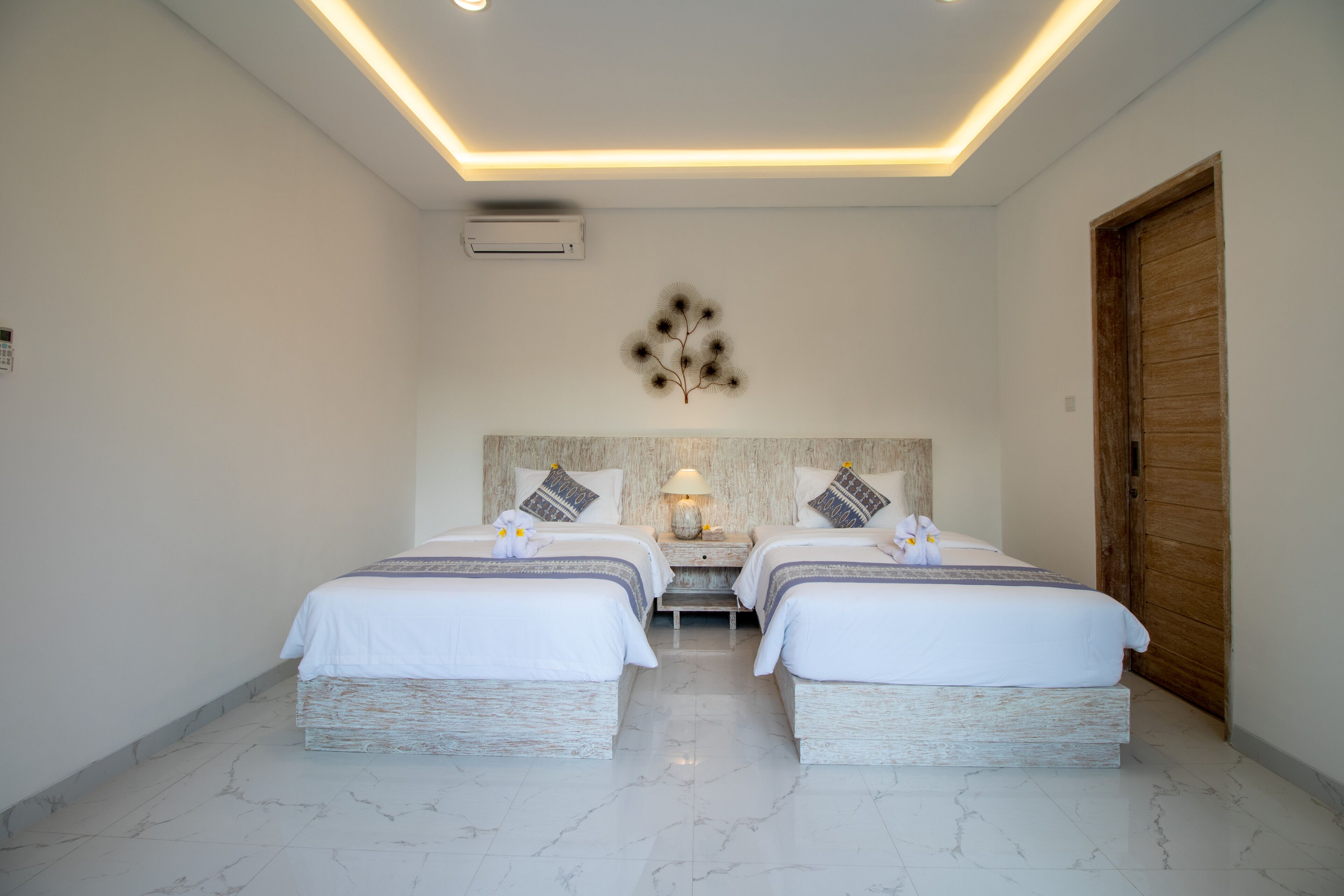 A hotel room with two beds, a wooden door, and a ceiling light fixture.
