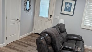 A living room with a black leather sofa, a white door, a window with blinds, and a framed picture on the wall. - GORGEOUS 1 BED GUEST HOME (Alpine)