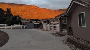 A residential area with a paved driveway leading to houses, surrounded by a white picket fence, and a mountain in the background. - GORGEOUS 1 BED GUEST HOME (Alpine)