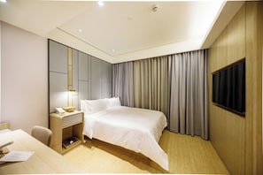 Une chambre d’hôtel moderne équipée d’un lit, d’une table de chevet, d’une lampe et d’un téléviseur fixé au mur.