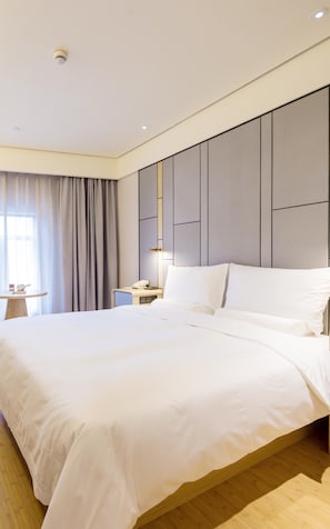 Une chambre d’hôtel moderne avec un grand lit, une table de chevet avec une lampe, une petite table avec un téléphone et une tasse, et une fenêtre avec des rideaux.