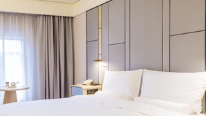 Una habitación de hotel moderna con una cama grande, una mesita de noche con una lámpara, una pequeña mesa con un teléfono y una taza, y una ventana con cortinas.