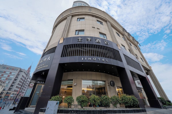 Un hôtel à la façade incurvée, doté de grandes fenêtres et d’une enseigne indiquant qu’il s’agit d’un hôtel de la chaîne Jihotel.