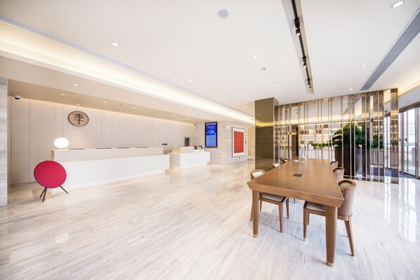 A modern hotel lobby with a reception desk, a large wooden conference table, and a glass partition.