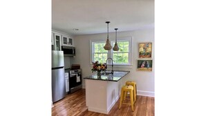 A kitchen with wooden flooring, a central island, yellow bar stools, a refrigerator, an oven, and a window with a view. - The Carriage House "The Entire Place (Abingdon)