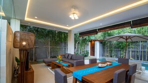 A modern indoor space with a wooden dining table, grey sofas, and a large umbrella. - Sayang Sanur Villa VII (Denpasar)