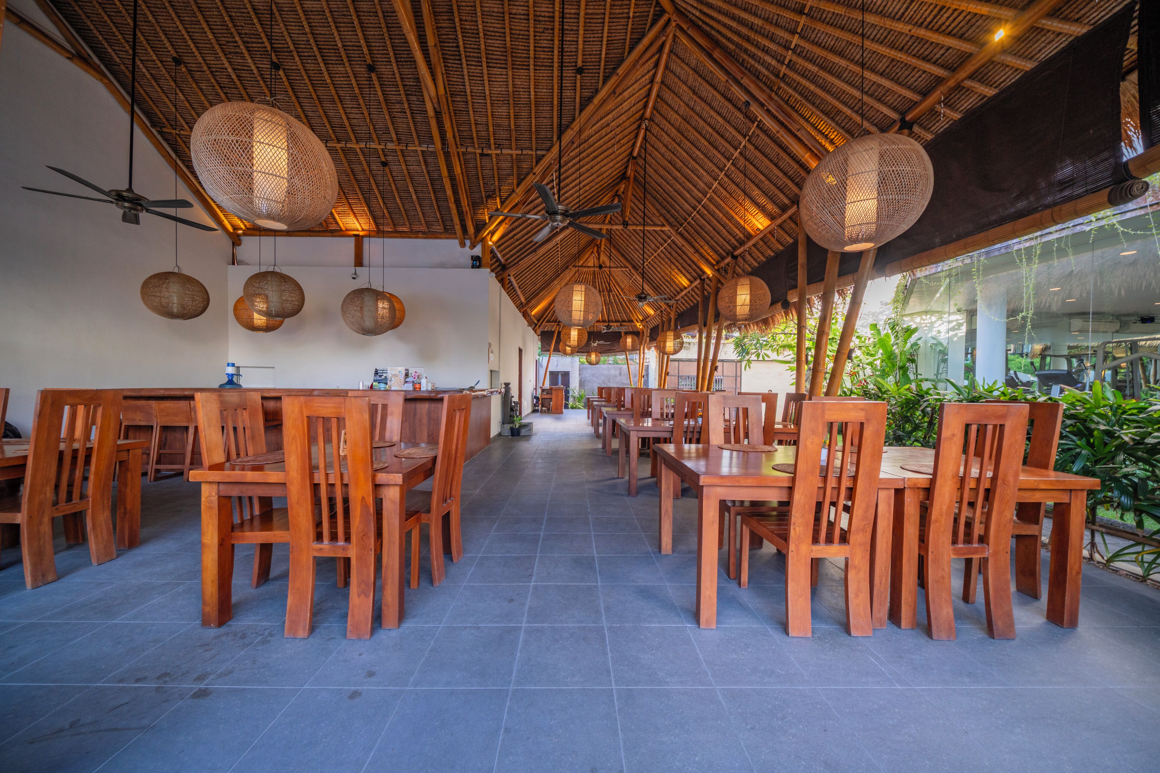 A restaurant with wooden tables and chairs, a tiled floor, and a thatched roof.