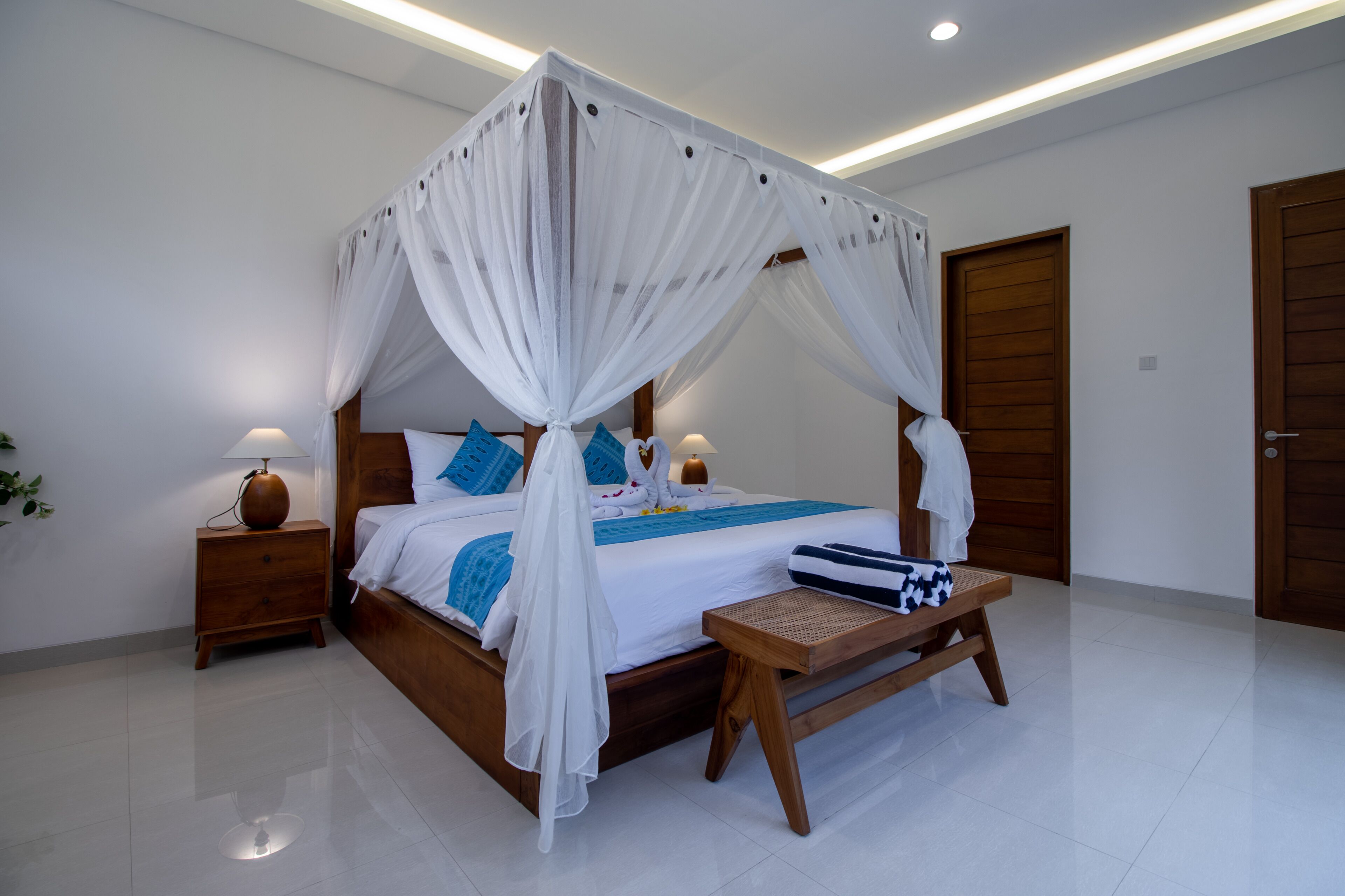 A bedroom with a four-poster bed, wooden nightstands, a bench, and a door.