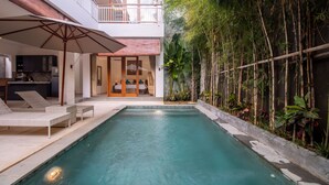Ein modernes Haus mit Swimmingpool, Liegestühlen und einem Balkon.