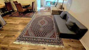 A living room with a sofa, a dining table with chairs, a large rug, and a TV on the wall. - Sherman Oaks Cozy Guest House  (Sherman Oaks)