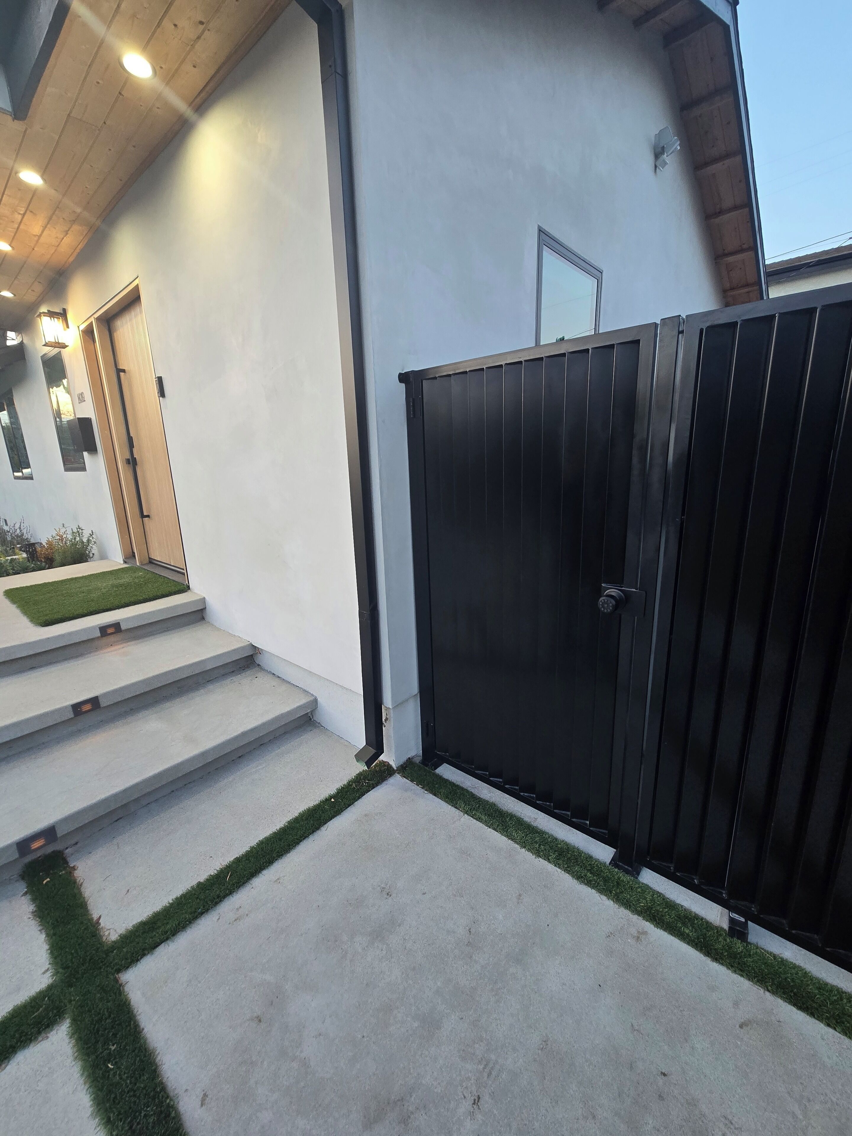 A modern building with a concrete staircase leading to a door, a metal gate, and a small lawn area.