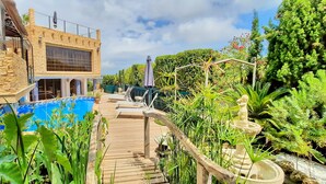 A pool area with a wooden deck, a stone wall, and a large window. - Villa Sun Carlos by Solidays - Benissa, Costa Blanca (Benissa)