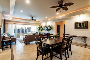 Uma sala de estar ampla com uma mesa de jantar, assentos confortáveis e um ventilador de teto.