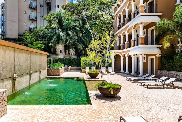 Piscina com água cristalina, rodeada por um terraço ladrilhado com espreguiçadeiras e vasos de plantas.