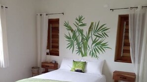 A bedroom with a bed, a nightstand, a bedside table, a window with curtains, and a potted plant.