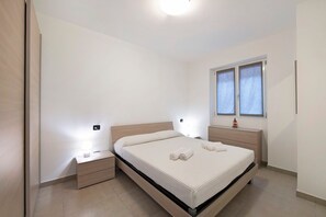 Un dormitorio con una cama, mesitas de noche, una lámpara de pared y una ventana.