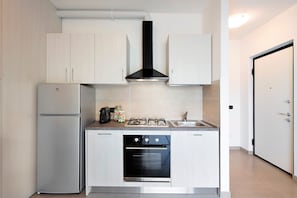 Una cocina compacta con refrigerador, estufa, horno y gabinetes blancos.