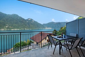 Un balcone con tavolo e sedie che si affaccia su un lago e montagne.