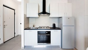 Een moderne keuken met witte kasten, een zwarte afzuigkap, een inbouwoven en een witte koelkast.