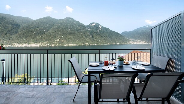 Een balkon met een eettafel, met uitzicht op een bergachtig landschap en een wateroppervlak.