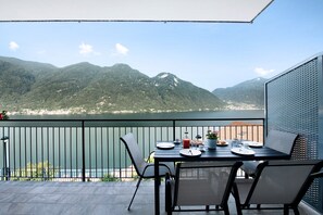 Een balkon met een eettafel, met uitzicht op een bergachtig landschap en een wateroppervlak.