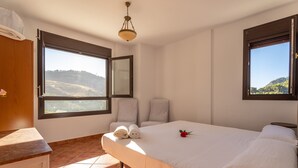 Une chambre à coucher avec un lit, deux fenêtres, un miroir, une chaise et une commode en bois.