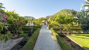 Un chemin de jardin menant à un bâtiment orné d’un drapeau, entouré de haies et de plantes bien entretenues.