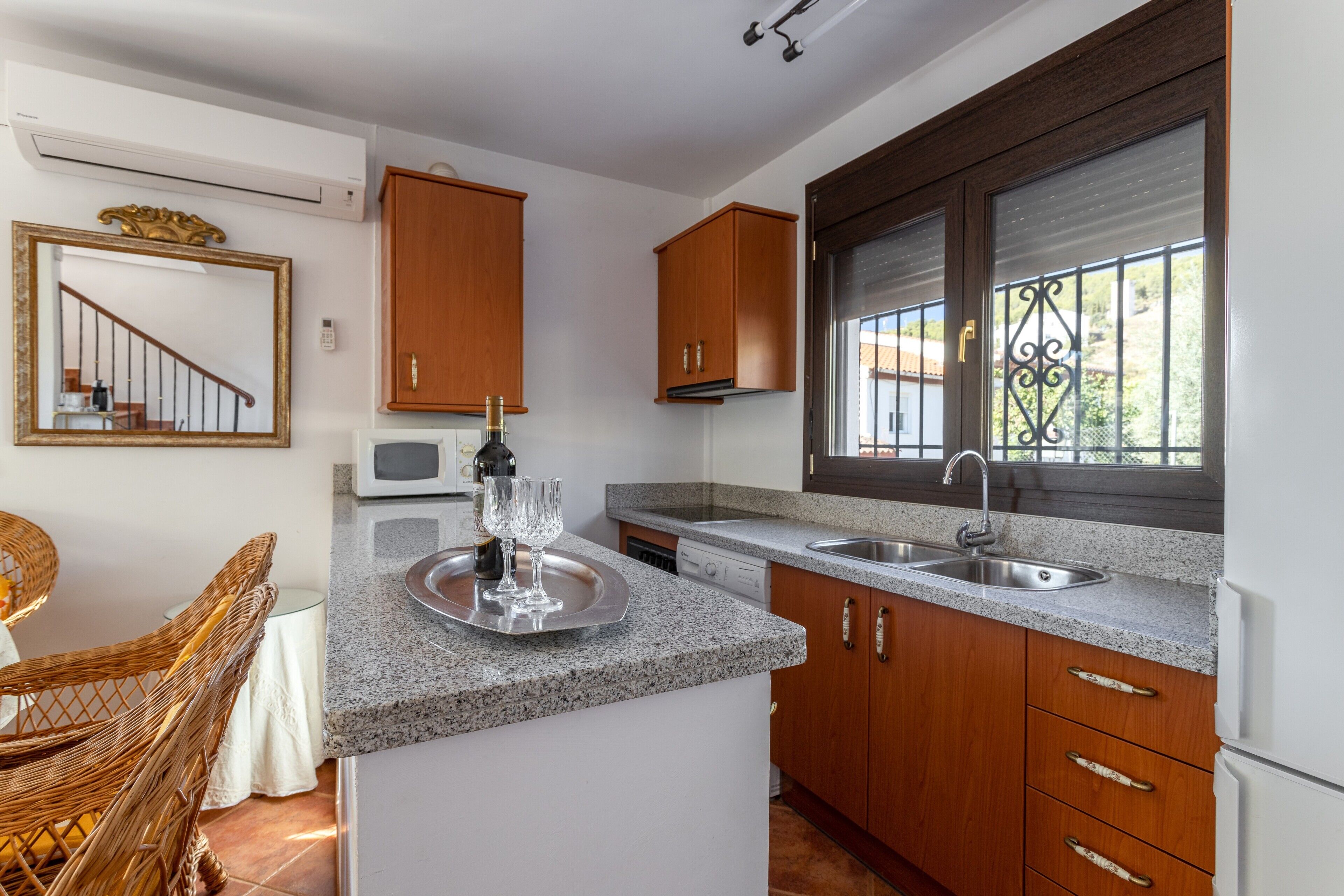 A kitchen with granite countertops, wooden cabinets, a built-in microwave, and a window with a metal grill.