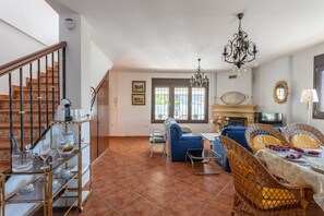 A spacious living room with a staircase, a fireplace, and a dining area with wicker furniture.