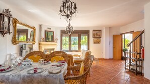 Un coin repas avec une table dressée pour quatre personnes, des chaises en osier, un lustre et une cheminée.