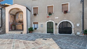 A building with a stone facade, arched doorways, and a tiled courtyard. - Apartment "Nonna Fina" with Lake & Mountain View, Shared Pool & Wi-Fi (Tignale)