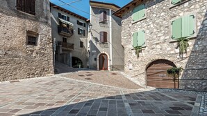 A narrow cobblestone street with stone buildings, a wooden door, and green shutters. - Apartment "Nonna Fina" with Lake & Mountain View, Shared Pool & Wi-Fi (Tignale)