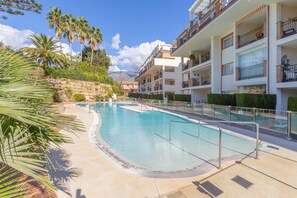 Una piscina con pared de piedra, palmeras y un edificio de varios pisos con balcones.