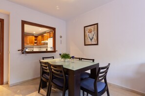 Un comedor con una mesa de vidrio, sillas de madera, una planta en maceta y un cuadro en la pared.